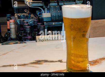Ein hohes Glas helles goldenes Bier, gekrönt mit einem dicken weißen Schaumkopf an einem ruhigen Platz an der Bar. Stockfoto