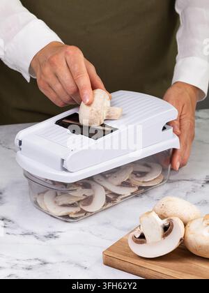Frau schneidet frische Steinpilze mit einer manuellen Mandolineschneidevorrichtung in dünne Scheiben und verwendet einen Behälter auf einer Marmorarbeitsplatte Stockfoto