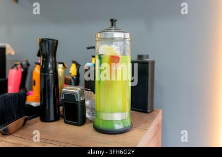 Nahaufnahme eines Friseurstischs mit bunten Kämmen in einem Glas Desinfektionsmittel, umgeben von Haarschneidern, Sprühflaschen, Bürsten und Pflegewerkzeugen Stockfoto