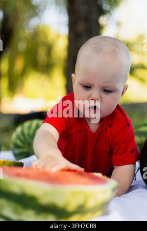 Familienpicknick in der Natur mit Mutter und Baby, die draußen an einem sonnigen Sommertag eine Wassermelone genießen. Stockfoto