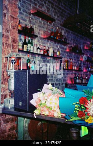 Zwei Blumensträuße auf einer DJ-Kabine neben einem Lautsprecher in einer Cocktailbar, mit analogem Blitz für eine authentische Nachtclub-Atmosphäre aufgenommen. Stockfoto