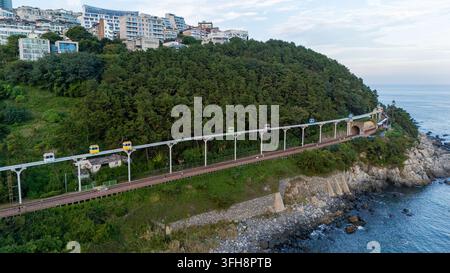 Farbenfrohe Himmelskapseln, die auf einer erhöhten Strecke entlang der Mipo-Küste von Busan fahren und städtische Gebiete mit malerischen Aussichten verbinden Stockfoto