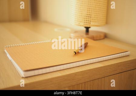 Arbeitsplatz mit einem Notizbuch und einem Stift auf einem Holzschreibtisch und einer Lampe Stockfoto