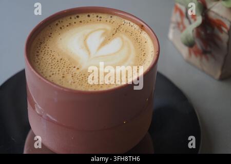 Kaffee serviert in einer rosa Tasse mit Herzdesign auf dem Schaum Stockfoto