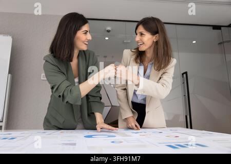 Aufgeregte erwachsene weibliche Teamkollegen machen einen Fauststoß über analytische Berichte Stockfoto