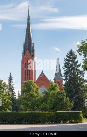 TURKU, FINNLAND - 24. JUNI 2026: Die rote Backsteinkirche Michael mit ihrem hohen Turm, eingerahmt von belaubten Ästen. Stockfoto