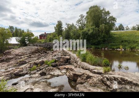 Alte Steinbrücke über ein trockenes felsiges Flussbett mit einer roten Holzscheune am Ufer. Stockfoto