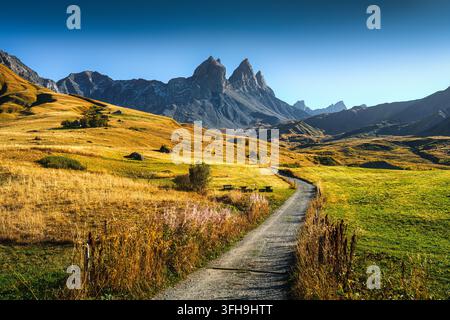 Pittoreske alpine Landschaft eines sich windenden Schotterweges, der durch ein goldenes Tal mit berühmten Berggipfeln unter blauem Himmel an einem sonnigen Herbsttag in Aigui führt Stockfoto