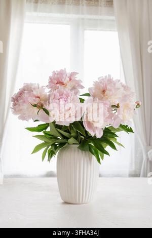 Großer Strauß rosafarbener Pfingstrosen in weißer Vase am Fenster Stockfoto