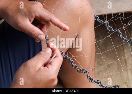 Eine Hand repariert ein Fischernetz mit Kette und Faden in der Nähe des Wassers Stockfoto
