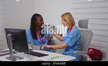 Mehrfarbige Krankenschwestern umarmen sich und lächeln im Krankenhausbüro Stockfoto