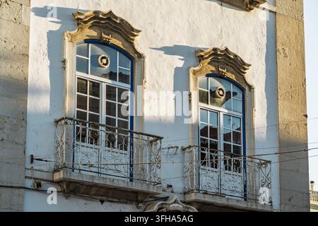 Ansicht einer traditionellen portugiesischen Gebäudefassade mit kunstvoll verzierten steingefassten Fenstern und schmiedeeisernen Balkonen in Setubal, Setubal, Portugal. Stockfoto