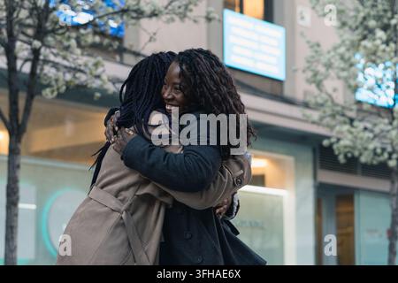 Zwei glückliche afroamerikanische Freundinnen teilen eine herzliche Umarmung auf einer Stadtstraße Stockfoto