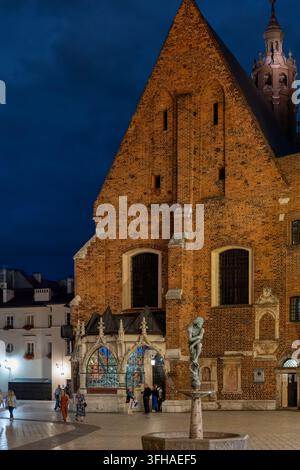 KRAKOW, POLEN – 5. JULI 2024: Beleuchtete Kirche der Heiligen Barbara und Zak-Brunnen auf dem Mariacki-Platz bei Nacht Stockfoto