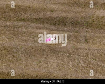 Luftbild einer Frau, die auf einem Heuballen in einem abgeernteten Feld in Lettland liegt. Stockfoto