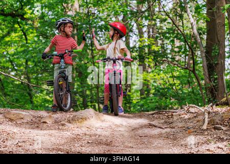 Zwei Kinder geben sich ein High-Five neben Fahrrädern auf einem sommerlichen Waldweg Stockfoto