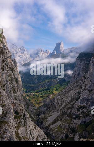 Blick auf den Naranjo de Bulnes-Gipfel, der über der tiefen Kalksteingeschwucht der Picos de Europa aufragt, mit tief hängenden Wolken, üppigen grünen Hängen und rugge Stockfoto