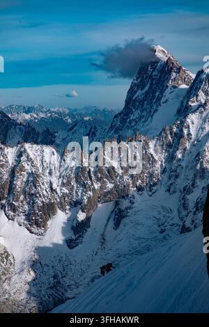 Blick auf den Mont Blanc mit schneebedeckten Gipfeln und zwei Bergsteigern, die einen steilen schneebedeckten Hang unter einem klaren blauen Himmel in Chamonix, Auvergne-Rhone-Alpes, Fr erklimmen Stockfoto