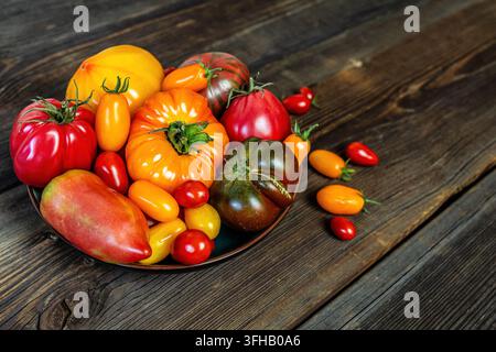 Verschiedene frische Heirloom-Tomaten in einer Schale auf einem rustikalen Holz-Hintergrund. Stockfoto