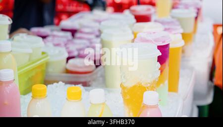 Farbenfrohe Frucht-Smoothies und -Säfte in Plastikbechern und Flaschen, die auf zerkleinertem Eis an einem Outdoor-Straßenmarkt ausgestellt sind, gekühlte Sommergetränke fo Stockfoto