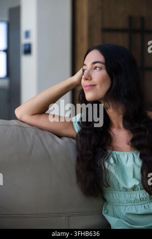 Frau liegt auf grauem Ledersofa zu Hause, trägt mintgrünes schulterfreies Oberteil, blickt nach rechts Stockfoto