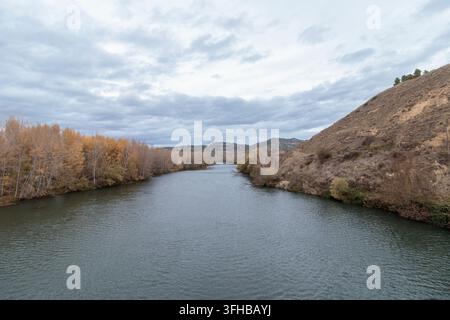 Ebro-Fluss schlängelt sich durch Hügel und Herbstbäume unter einem bewölkten Himmel Stockfoto