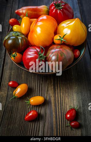 Verschiedene frische Heirloom-Tomaten in einer Schale auf einem rustikalen Holz-Hintergrund. Stockfoto