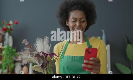 Floristin mit grüner Schürze hält Smartphone und Strauß aus getrockneten Gräsern und Eukalyptus im Blumengeschäft-Studio; Freude an kleinen Unternehmen. Stockfoto