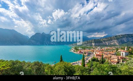Panoramarblick auf das Dorf Torbole sul Garda am Gardasee mit Bergkulisse und dramatischem bewölktem Himmel. Nago Torbole, Trentino, Italien Stockfoto