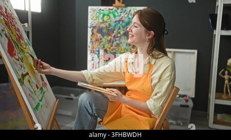 Frauenmalerin hält Pinsel und Palette und malt auf Leinwand, Hand greift zu, um Farbe im Atelier aufzutragen; konzentrierte Kreativität. Stockfoto