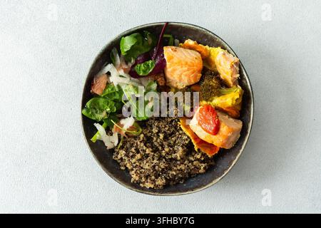 Eine Quinoa-Schüssel ist gefüllt mit gebackenem Lachs, Brokkoli, Tomaten und einem frischen Salat. Dieses Gericht eignet sich gut zum Frühstück oder Mittagessen und ist reich an Eiweiß und Stockfoto