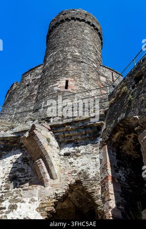Alte runde Turm der mittelalterlichen Festung erhebt sich über zerfallene Steinmauern, niedrigwinklige Vertikale Aufnahme unter hellem Sommerhimmel Stockfoto