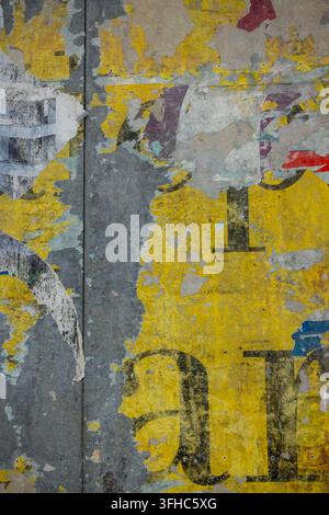 Verwitterte urbane Wand bedeckt mit zerrissenen Plakaten, verblassten Zahlen und geschichteten gelben, blauen, grauen und roten Papiertexturen Stockfoto