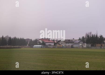 Vorstadthäuser stehen hinter einem weiten grasbewachsenen Feld an einem düsteren Tag und schaffen eine friedliche Szene, die den ruhigen Übergang zwischen l Stockfoto