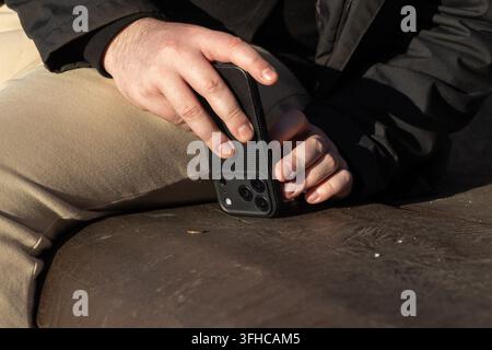 Nahaufnahme von menschlichen Händen, die ein schwarzes Smartphone mit mehreren Kameralinsen halten, das auf einer Holzoberfläche ruht und digitale Kommunikation und jeden verkörpert Stockfoto
