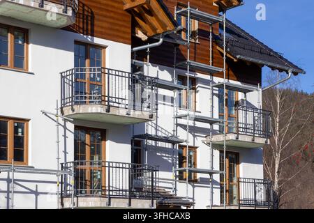 Fassade eines zeitgenössischen Wohngebäudes mit Balkonen, weißem Putz und Holzelementen, mit Gerüst für laufende Bauarbeiten, Schild Stockfoto