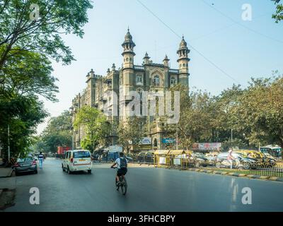 Straßenszene beim Betreten von Colaba im Süden Mumbais, Maharashtra, Indien, mit Verkehr, der an einem historischen verzierten Eckgebäude vorbeifährt Stockfoto
