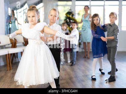 Begeisterte Teenager, Mädchen und Jungen in eleganten Outfits, die in einem mit Weihnachtsdekoration geschmückten Studio Partnertanzschritte üben, unter Gu Stockfoto