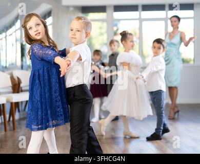 Begeisterte Teenager, Mädchen und Jungen in eleganten Outfits, die in einem mit Weihnachtsdekoration geschmückten Studio Partnertanzschritte üben, unter Gu Stockfoto