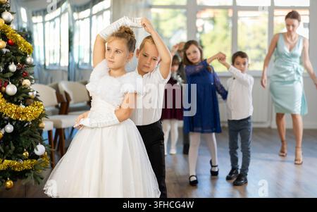 Begeisterte Teenager, Mädchen und Jungen in eleganten Outfits, die in einem mit Weihnachtsdekoration geschmückten Studio Partnertanzschritte üben, unter Gu Stockfoto