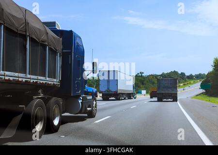 Mehrere Lastwagen fahren auf einer US-Autobahn in einer ländlichen Gegend mit offenem Raum und grünen Bäumen. Stockfoto