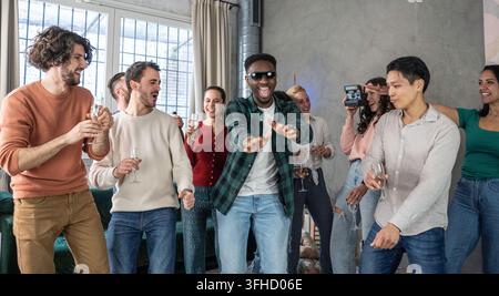 Verschiedene junge Freunde tanzen und lachen zusammen während einer energiegeladenen House-Party, während sie Getränke und unbeschwerte gesellige Zeit genießen. Eine authentische Szene der Gen Z Stockfoto