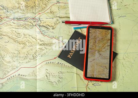 Ansicht von oben zeigt Reiseplanungsutensilien, darunter eine Papierkarte, ein Smartphone, das eine Karte anzeigt, einen Reisepass, ein Notizbuch und einen Stift, alle ausgebreitet Stockfoto