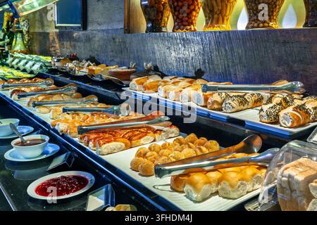 Luxushotel-Frühstücksbuffet mit einer großen Auswahl an frischen Broten, Gebäck und süßen Marmeladen, die auf einer eleganten Theke mit Servierzangen präsentiert werden. Stockfoto