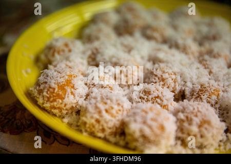 Ein detailliertes Makrofoto, das Reihen von traditionellen orangefarbenen Süßkartoffel-ondeh-ondeh (klepon) zeigt, die mit Kokosraspeln überzogen und auf einem gelben Teller arrangiert sind Stockfoto