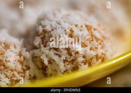 Ein detailliertes Makrofoto, das sich eng auf eine einzelne traditionelle orangefarbene Süßkartoffel ondeh-ondeh (klepon) konzentriert, die dick mit frisch geriebener Kokosnuss überzogen ist Stockfoto