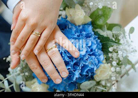 Eheringe, die Hände halten, in einem Blumenstrauß, mit Eheringen, Strauß mit blauen und, aus einer Nahaufnahme-Perspektive, mit blauen, weißen Akzenten Stockfoto