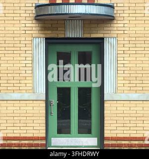 Die stromlinienförmige grüne Tür ist unter einem geschwungenen Metallüberdach auf einer gelben Ziegelfassade eingerahmt. Stockfoto