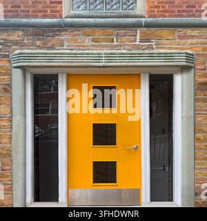 Mid-Century-Modern gelbe Tür mit quadratischen Fenstern an einer strukturierten Steinfassade. Stockfoto