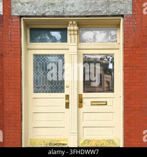 Gelbe Zwillings Türen mit Oberlichtern und messingfarbenen Griffen unter einem groben Steinsturz in einer roten Ziegel Fassade. Stockfoto